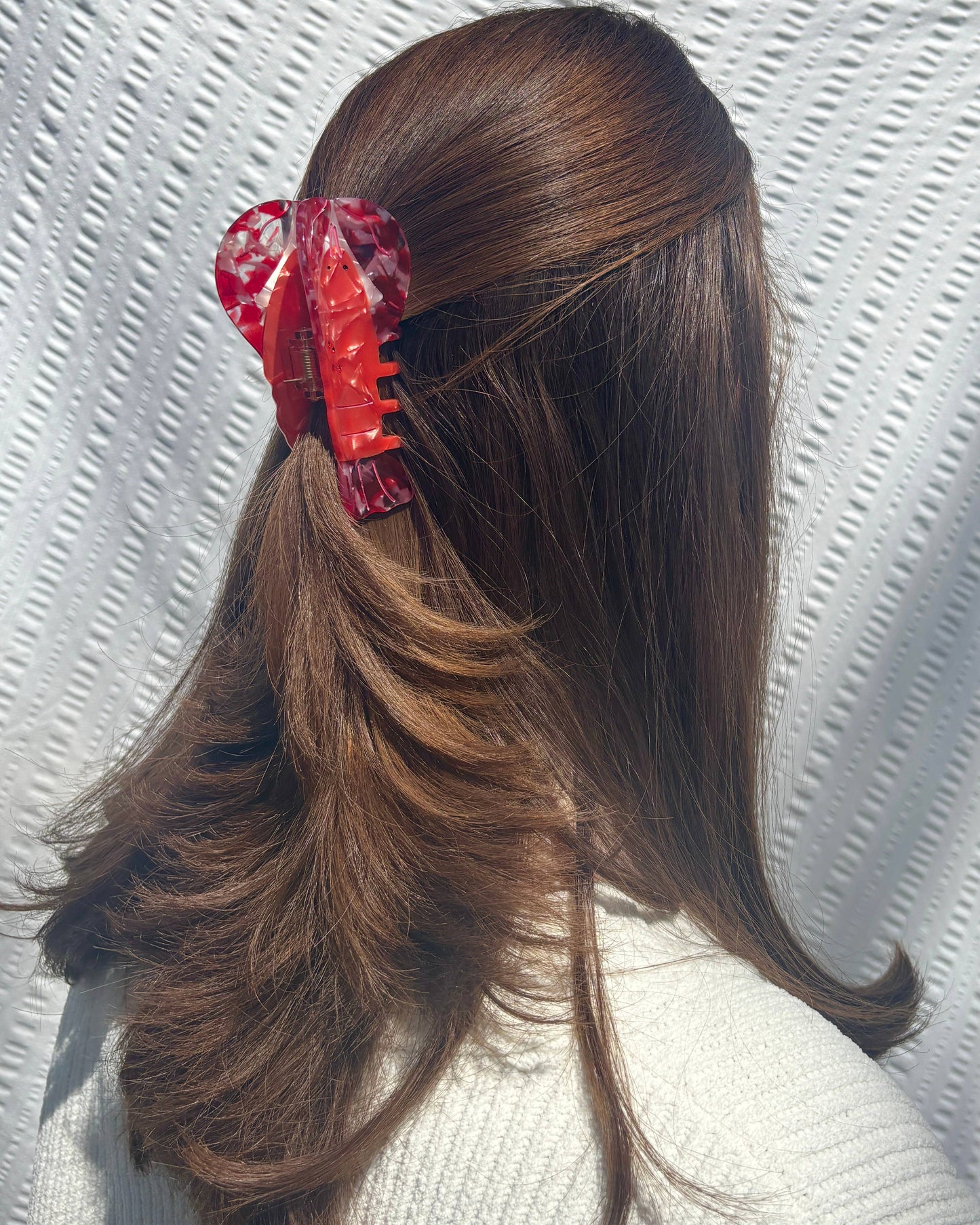 Woman with long brown hair pinned back with a red lobster hair clip on a textured white background