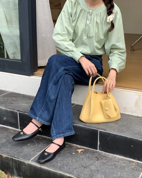 Person sitting on steps wearing a light green blouse, blue jeans, and black shoes, holding a yellow handbag.