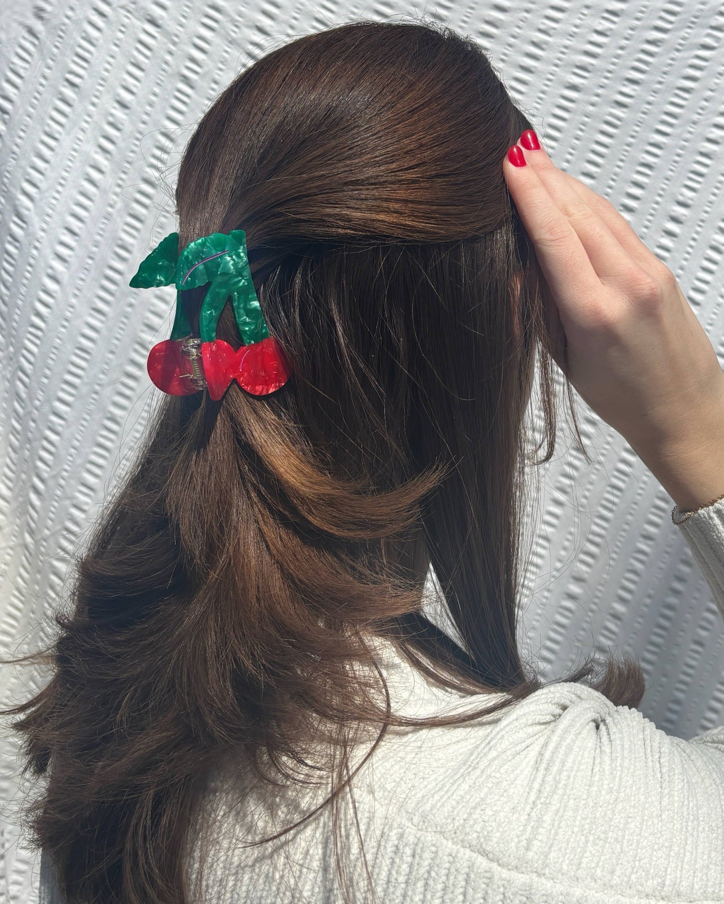 Back view of a woman wearing a cherry shaped hair clip in front of a textured white background