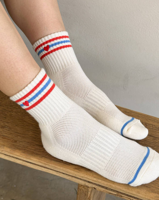 White socks with red and blue stripes worn by a person sitting on a wooden bench.