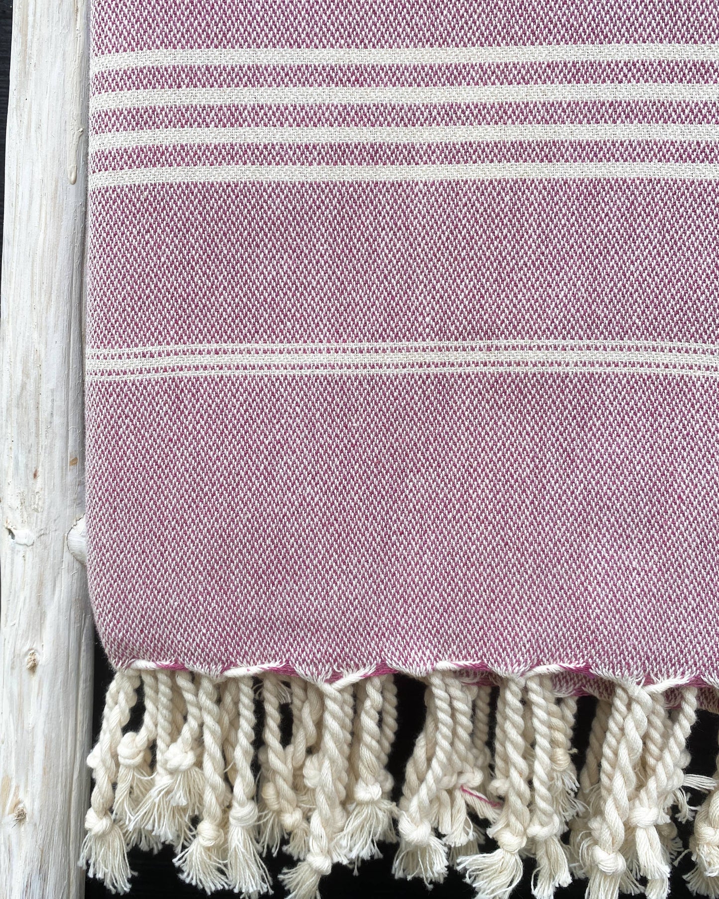 Purple towel with white stripes and tassels on a black background