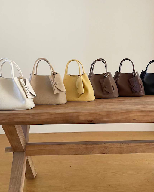 Six handbags in different colors arranged on a wooden surface.