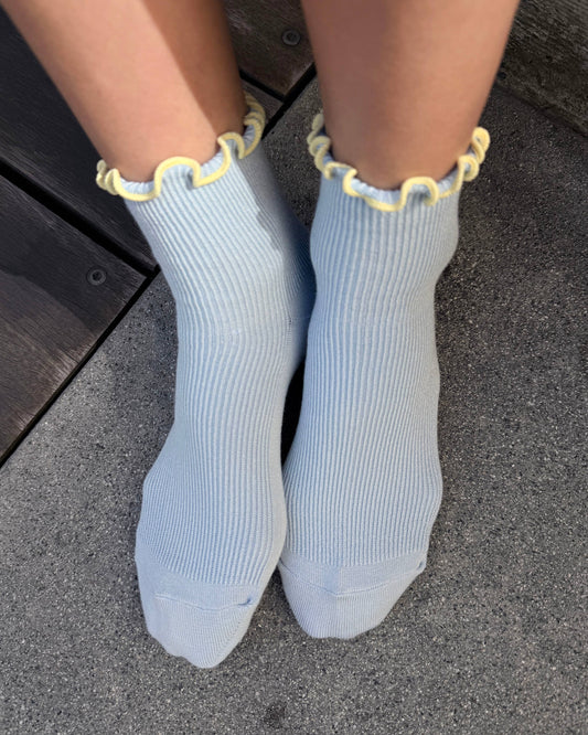 Light blue socks with yellow trim worn on a dark surface