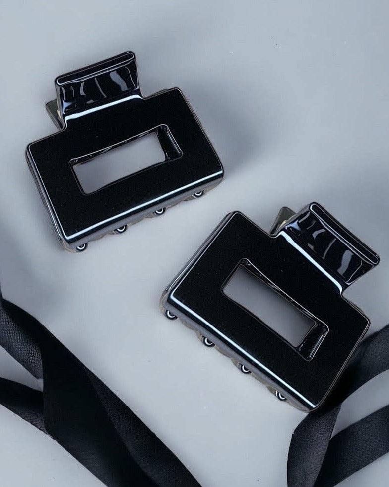 Two black belt buckles on a light gray background with black ribbons.