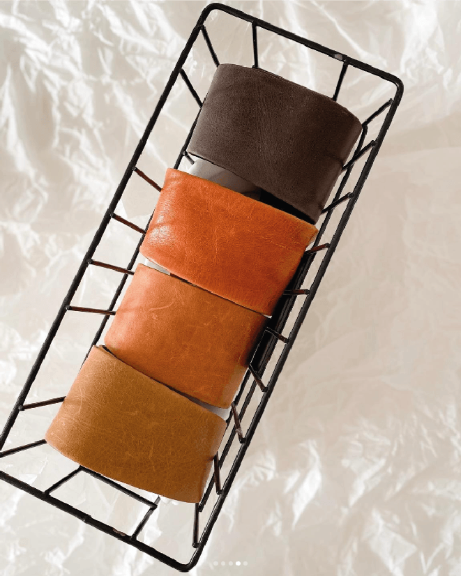Three cylindrical belts wrapped in brown paper on a black wire rack against a white background