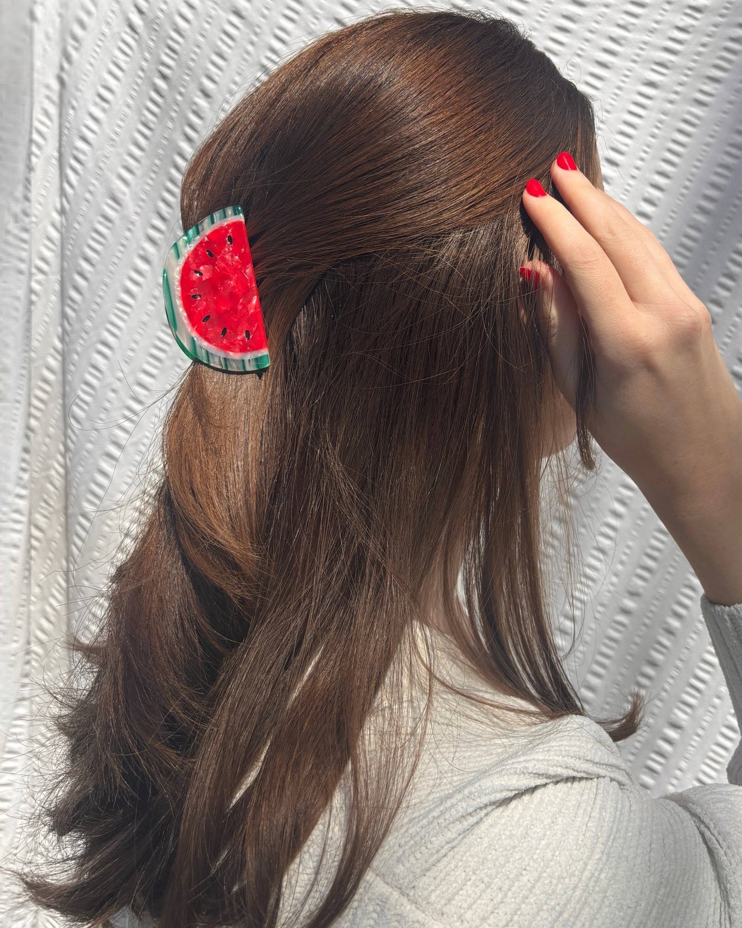 Person with a watermelon-themed hair clip in their hair against a textured white background