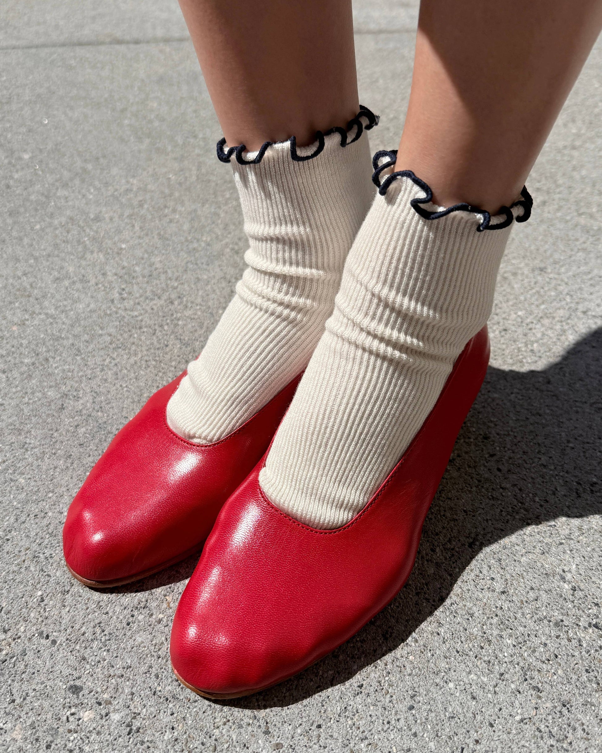 Red shoes worn with white socks on a concrete surface