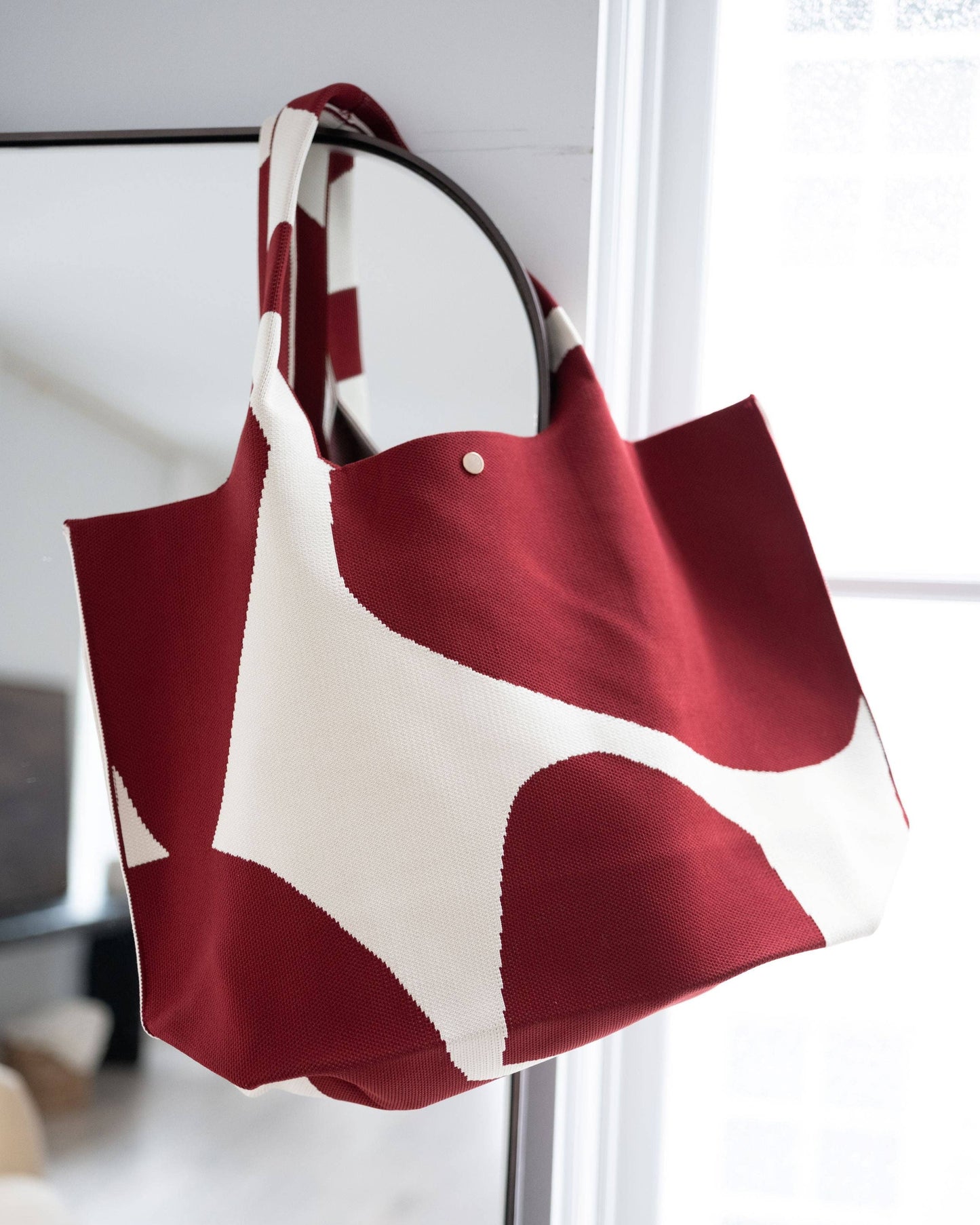 Red and white tote bag hanging on a metal rod indoors.