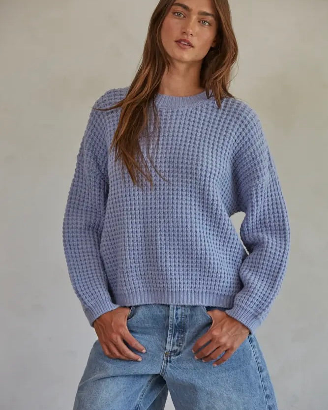 Model wearing By Together Waffle Knit Pullover In Dusty Blue wearing jeans on a beige background