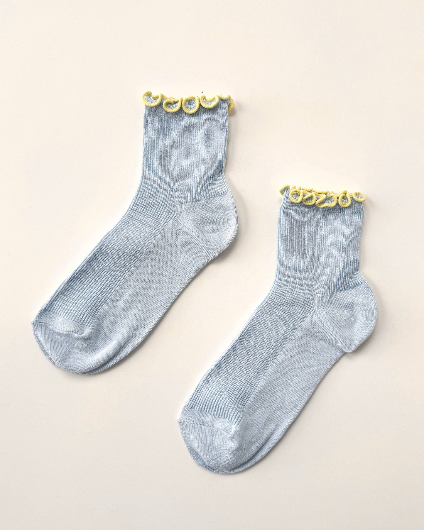 Pair of light blue socks with gold accents on a beige background