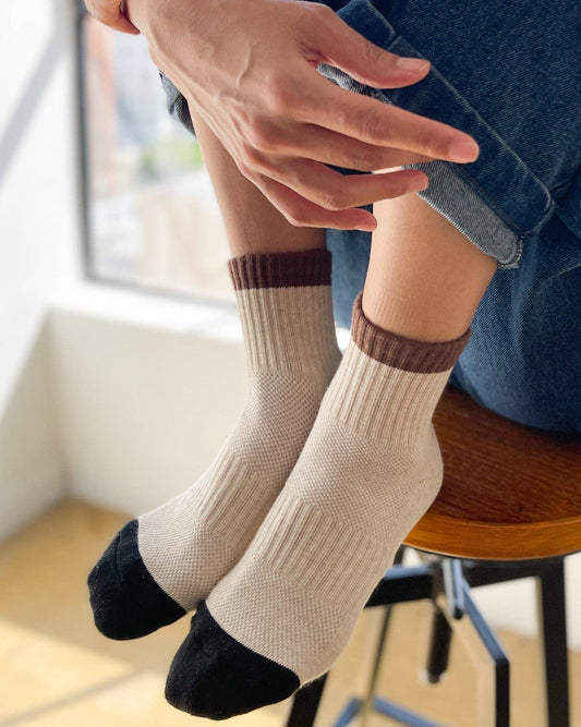 Person wearing beige socks with brown accents sitting on a chair.