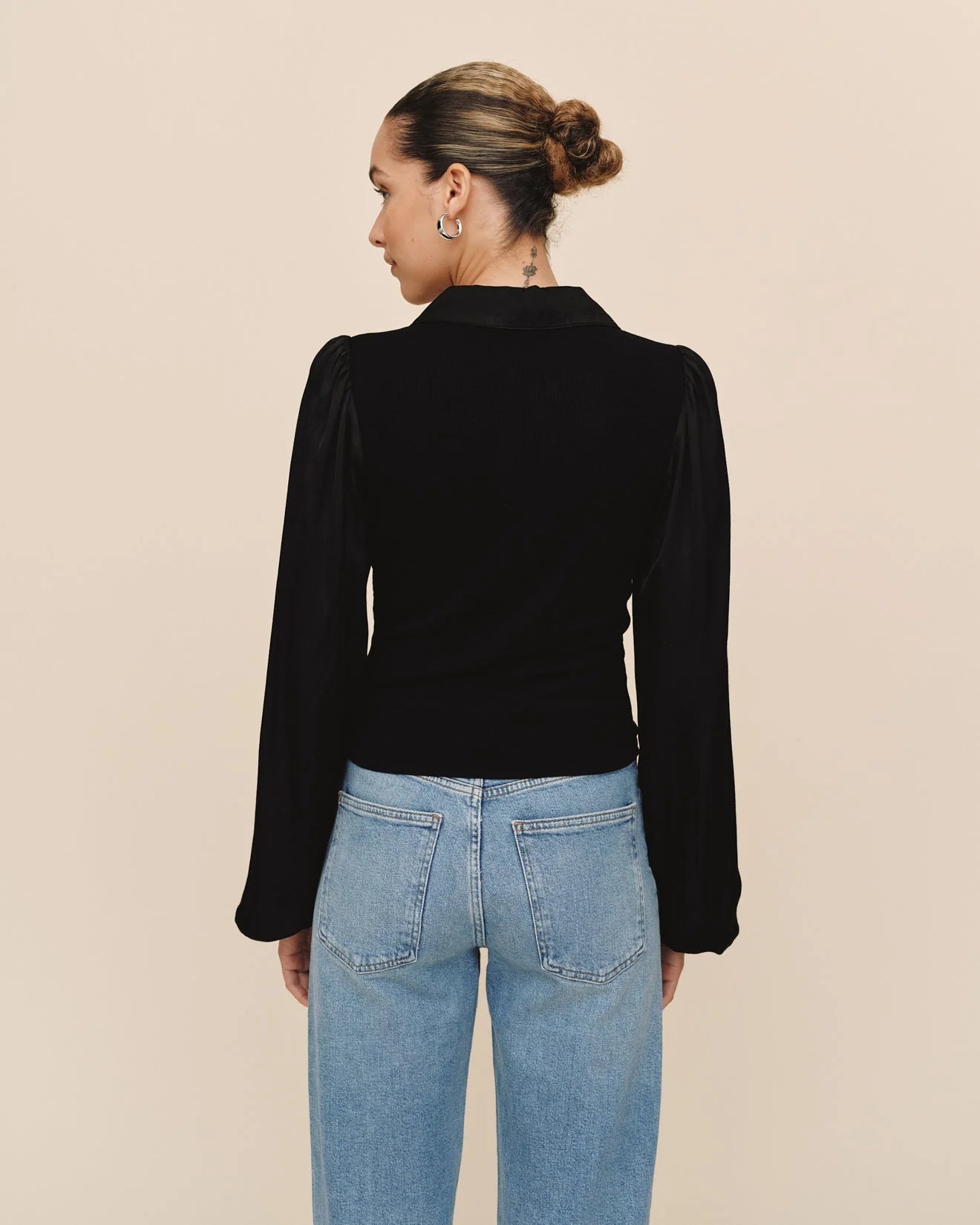 Person wearing a black velvet top and blue jeans on a beige background