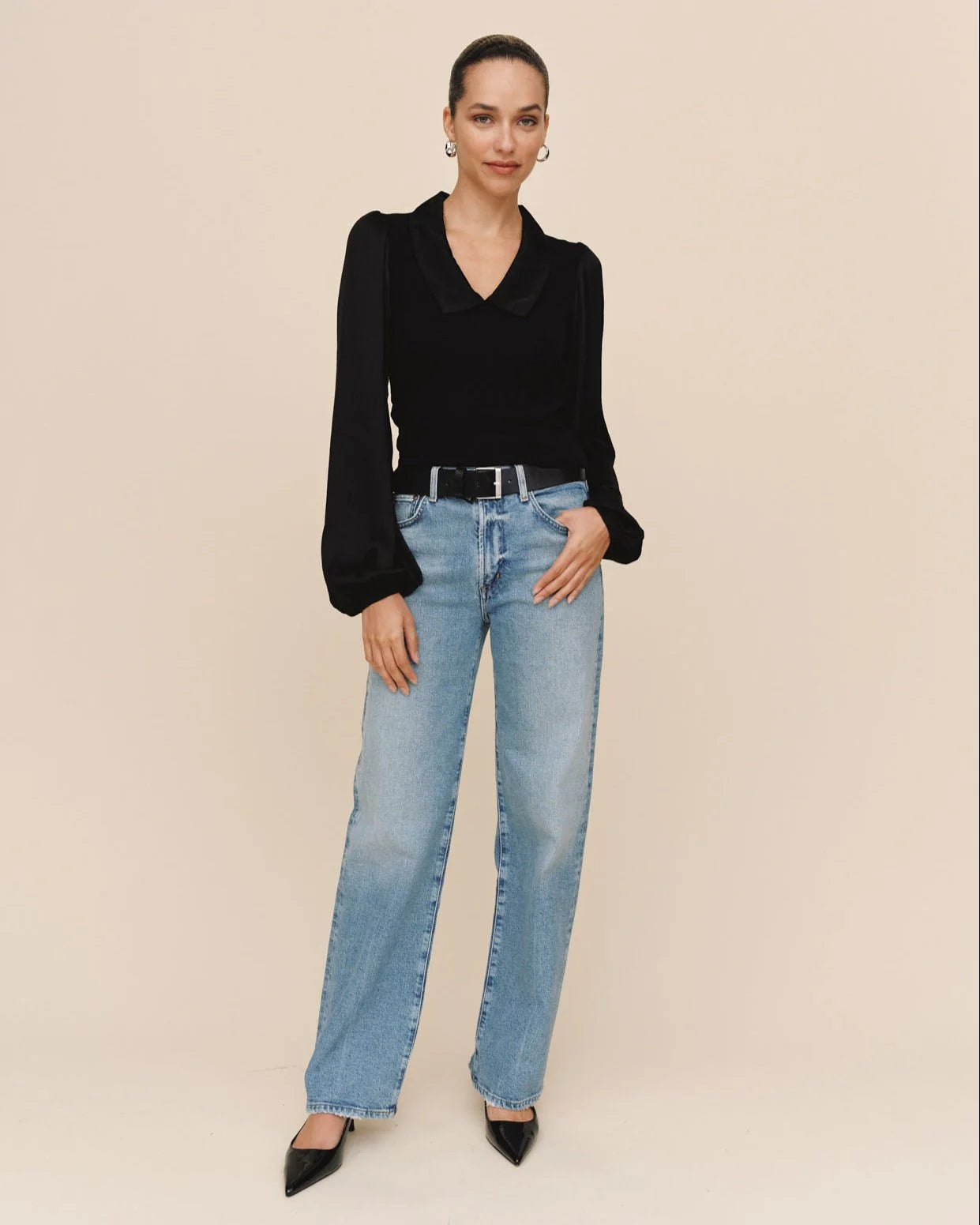 Woman wearing a black top and light blue jeans on a beige background