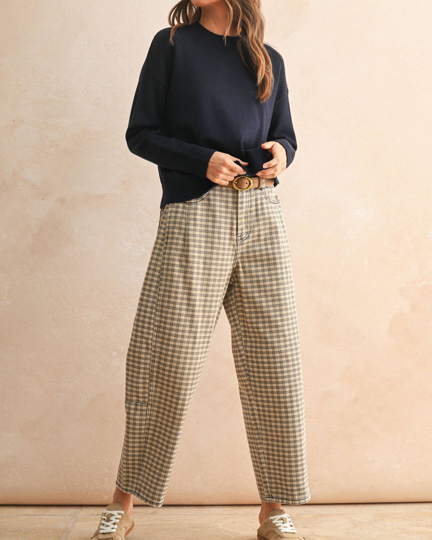 Woman wearing a navy sweater and plaid pants against a beige background