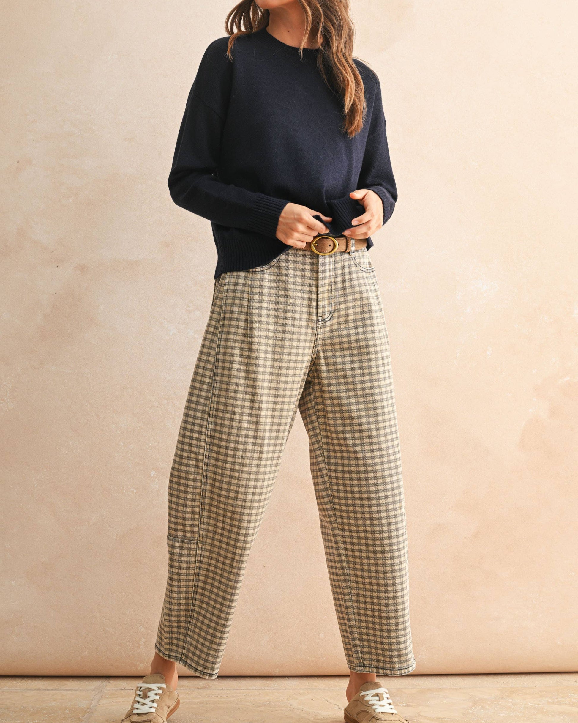 Woman wearing a navy sweater and plaid pants against a beige background