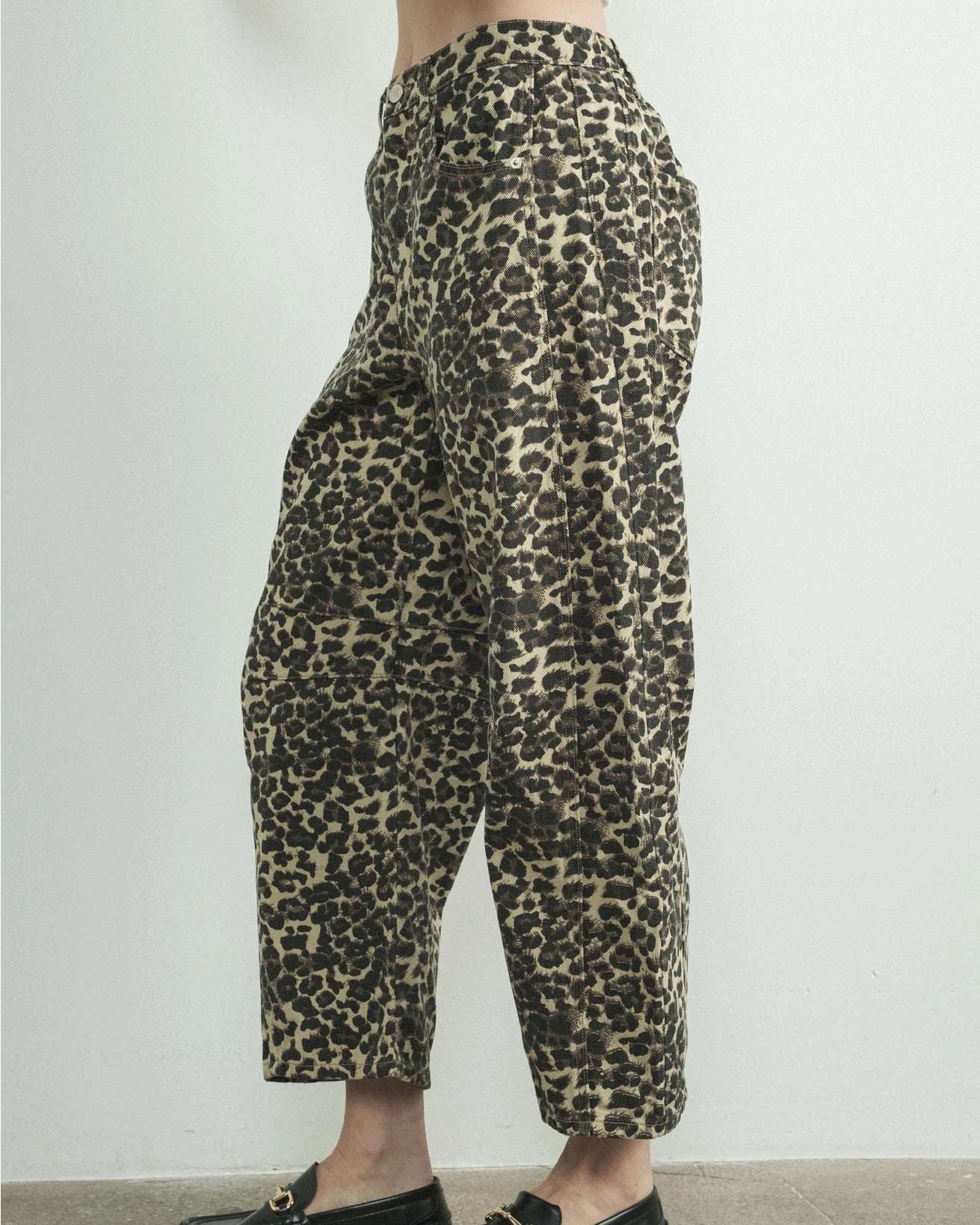 Side view of a model wearing a relaxed fit denim pant in leopard animal print with a white background.