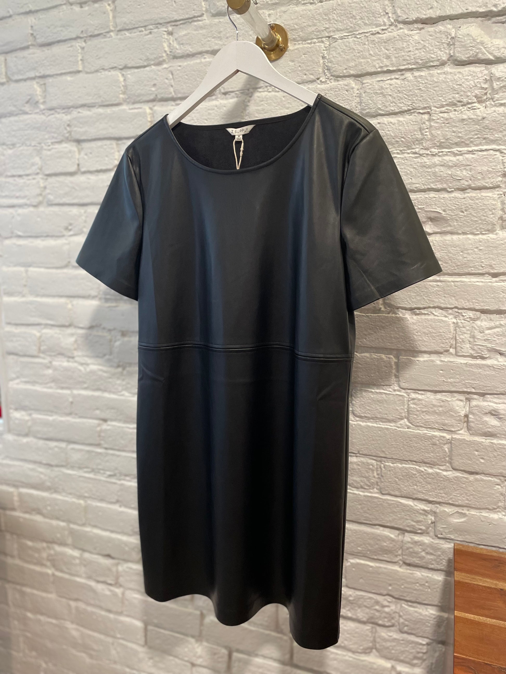 Z Supply London faux leather dress in black hanging on white brick.