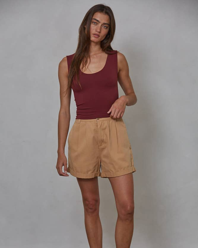 Front view of woman wearing a maroon tank top with beige shorts against a gray background