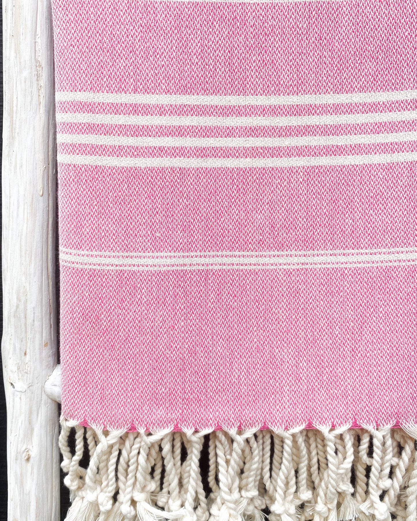 Pink towel with white stripes and fringes on a black background