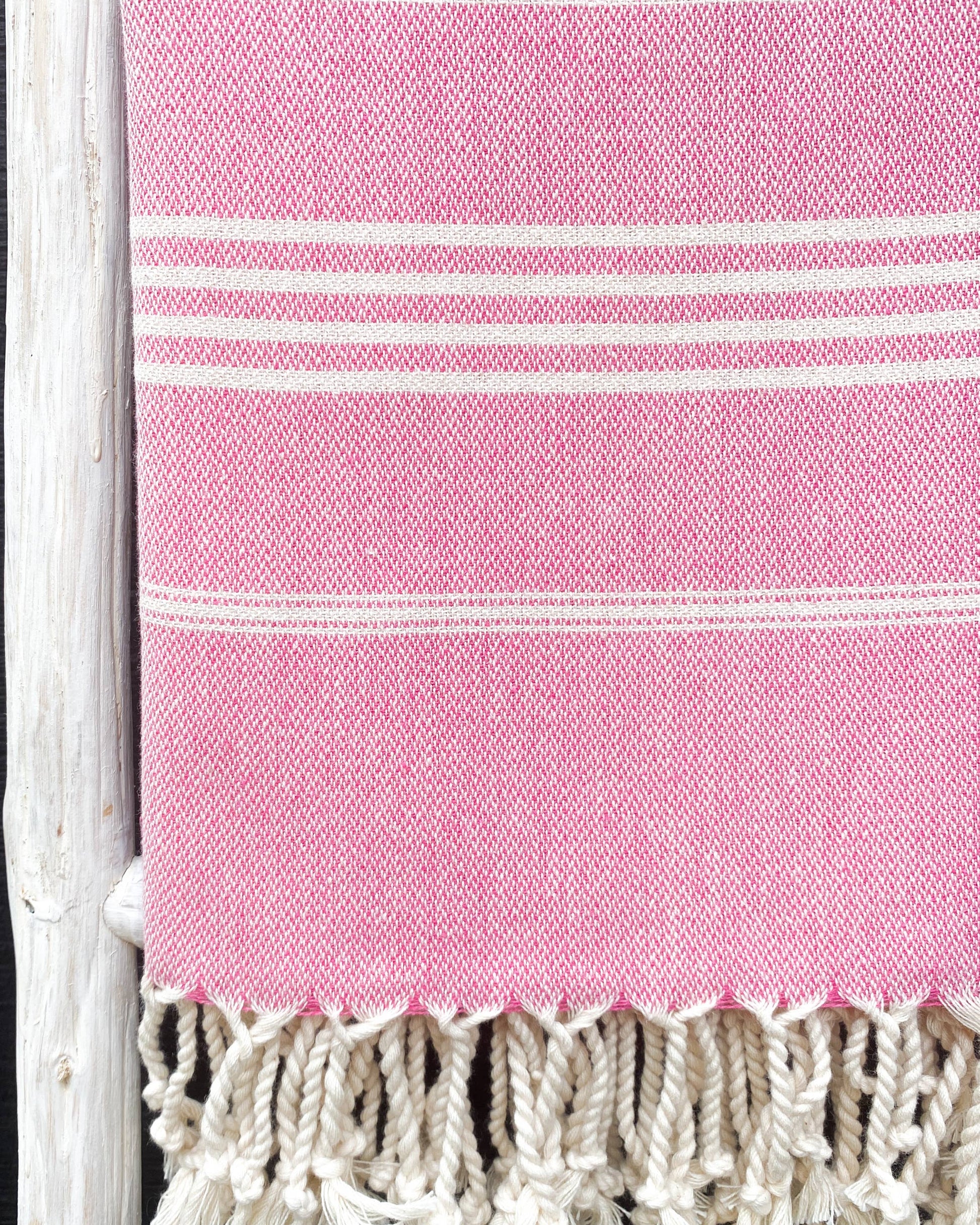 Pink towel with white stripes and fringes on a black background