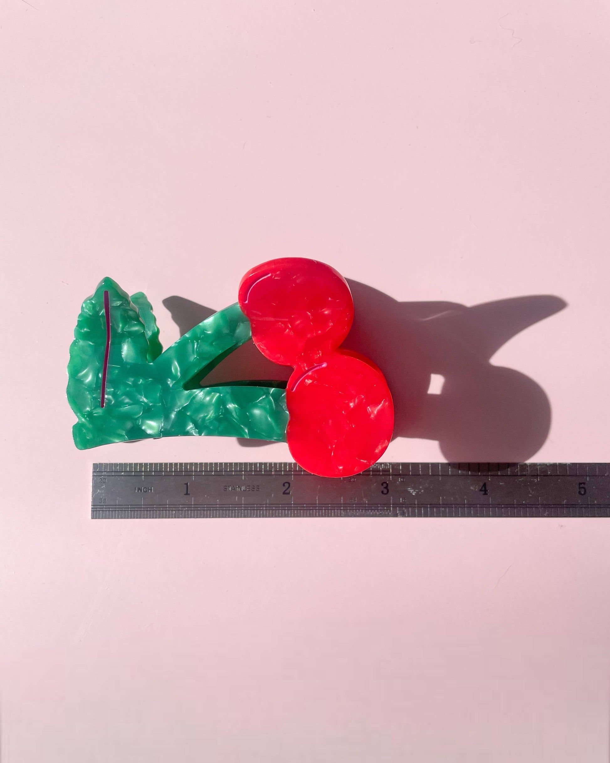 Side view of cherry shaped hair clip laying on a pink background