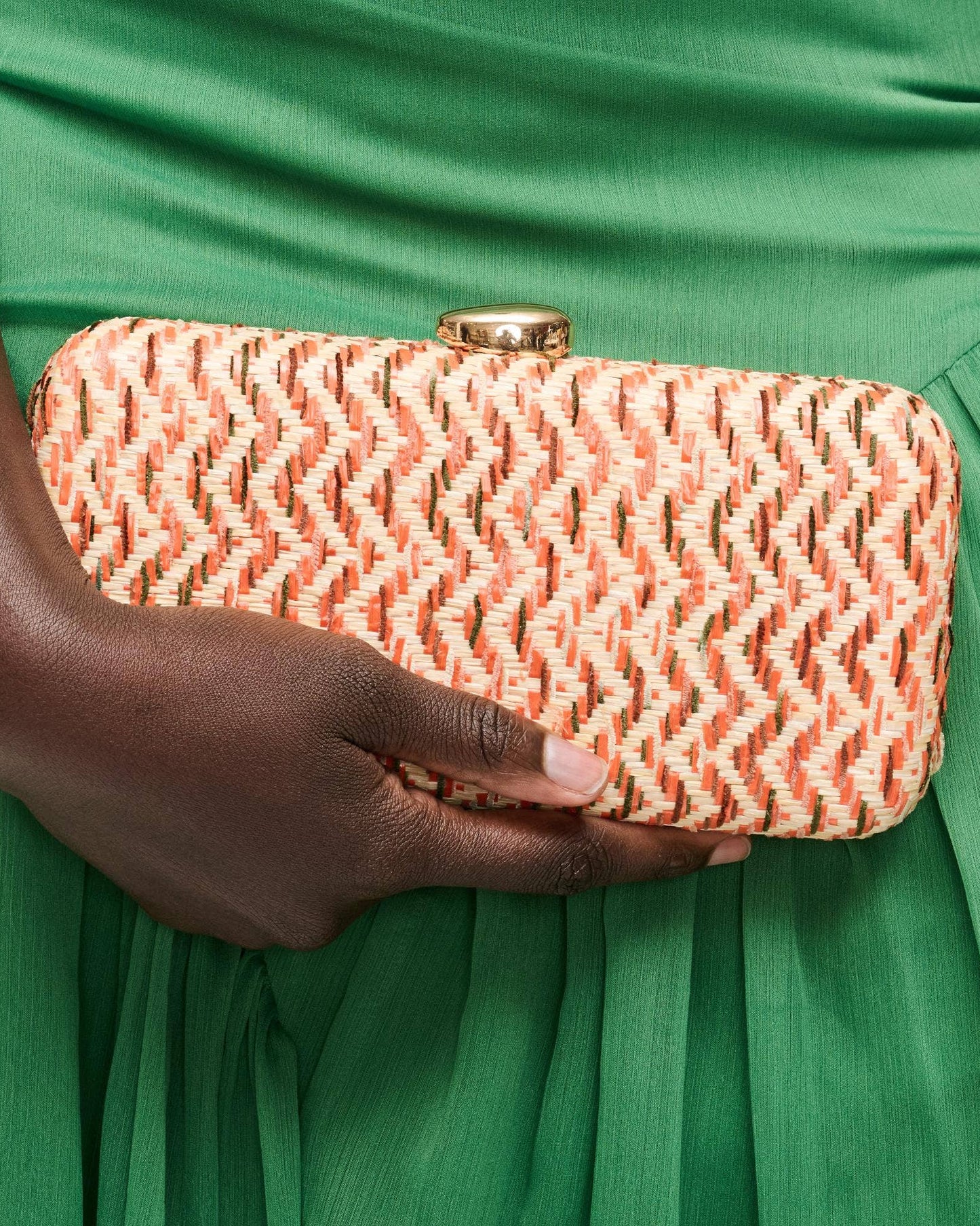 Hand holding a pink woven clutch against a green dress