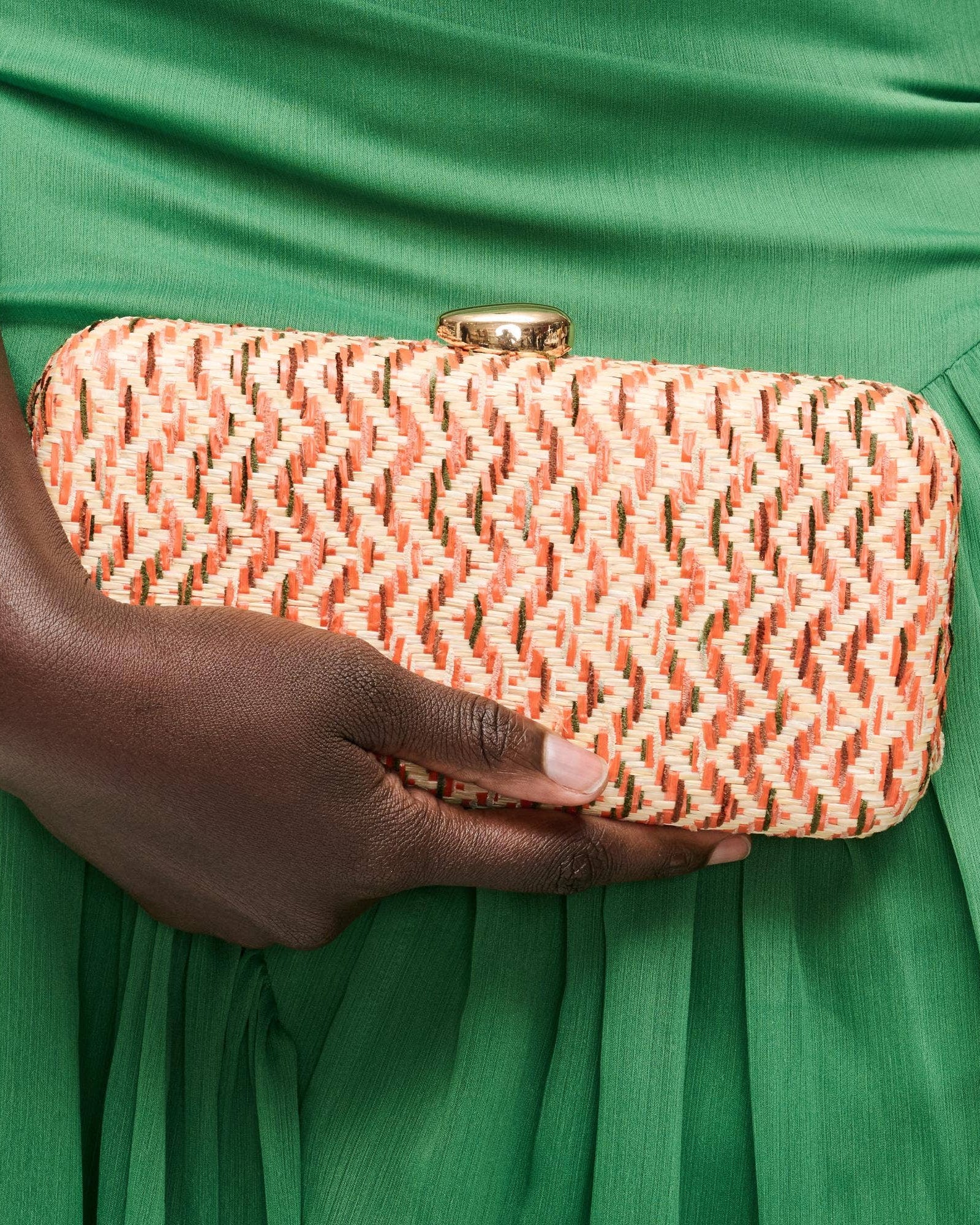Hand holding a pink woven clutch against a green dress