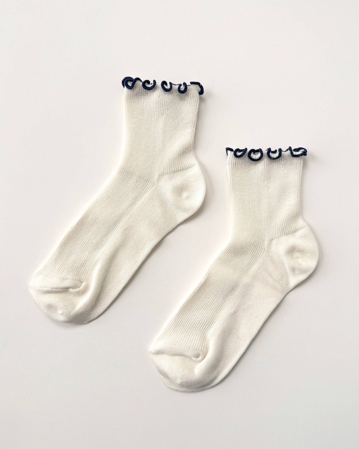 Pair of white socks with black heart-shaped tags on a light gray background