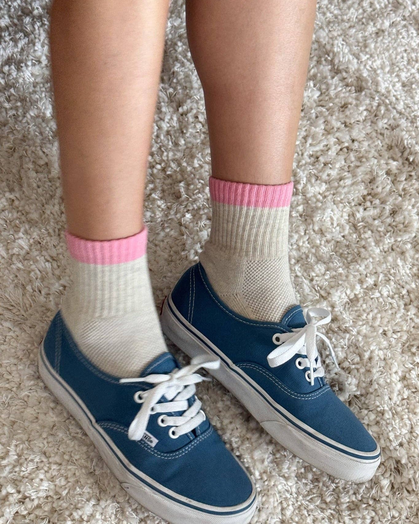 Blue sneakers with white laces worn on a textured surface