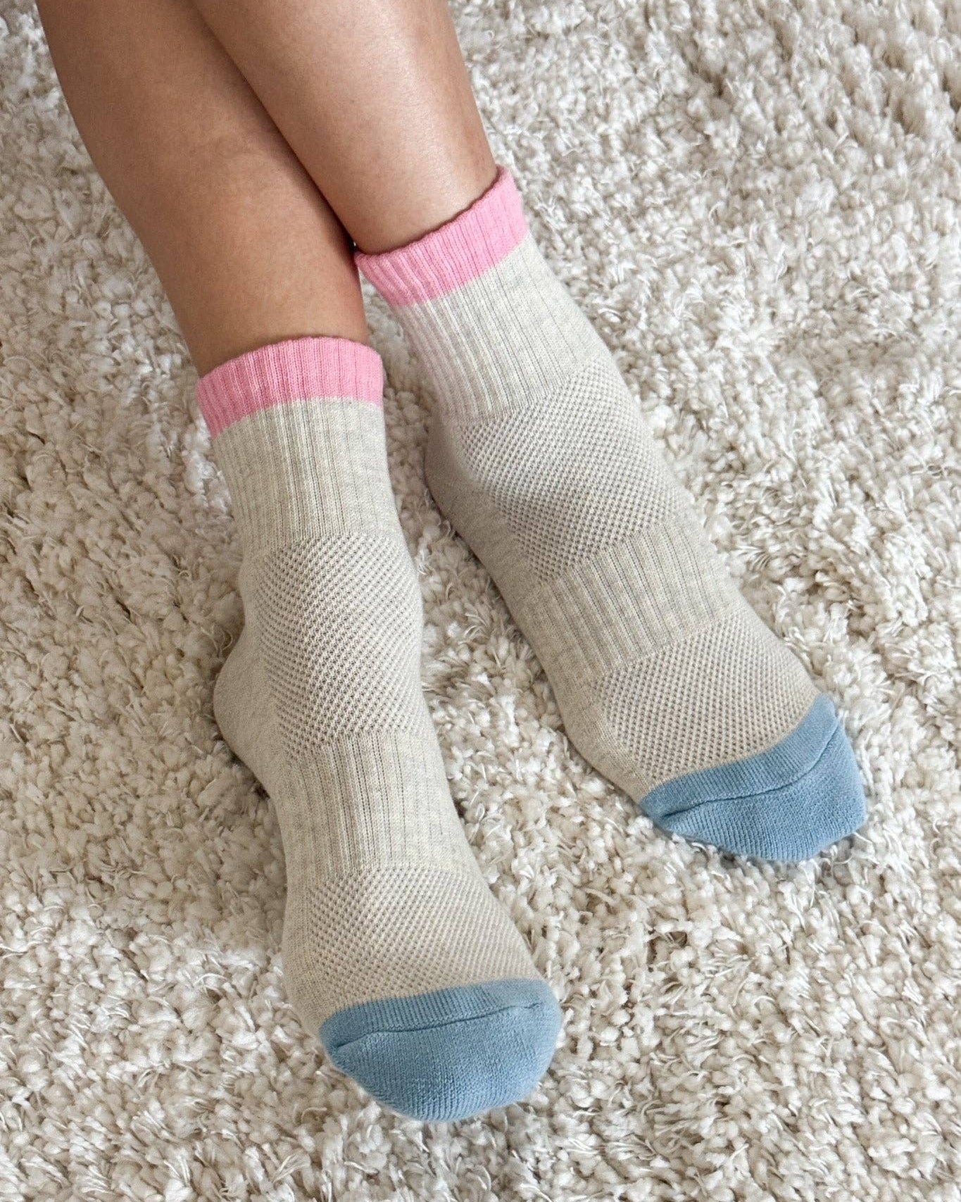 White socks with pink tops and blue toes on a beige carpet
