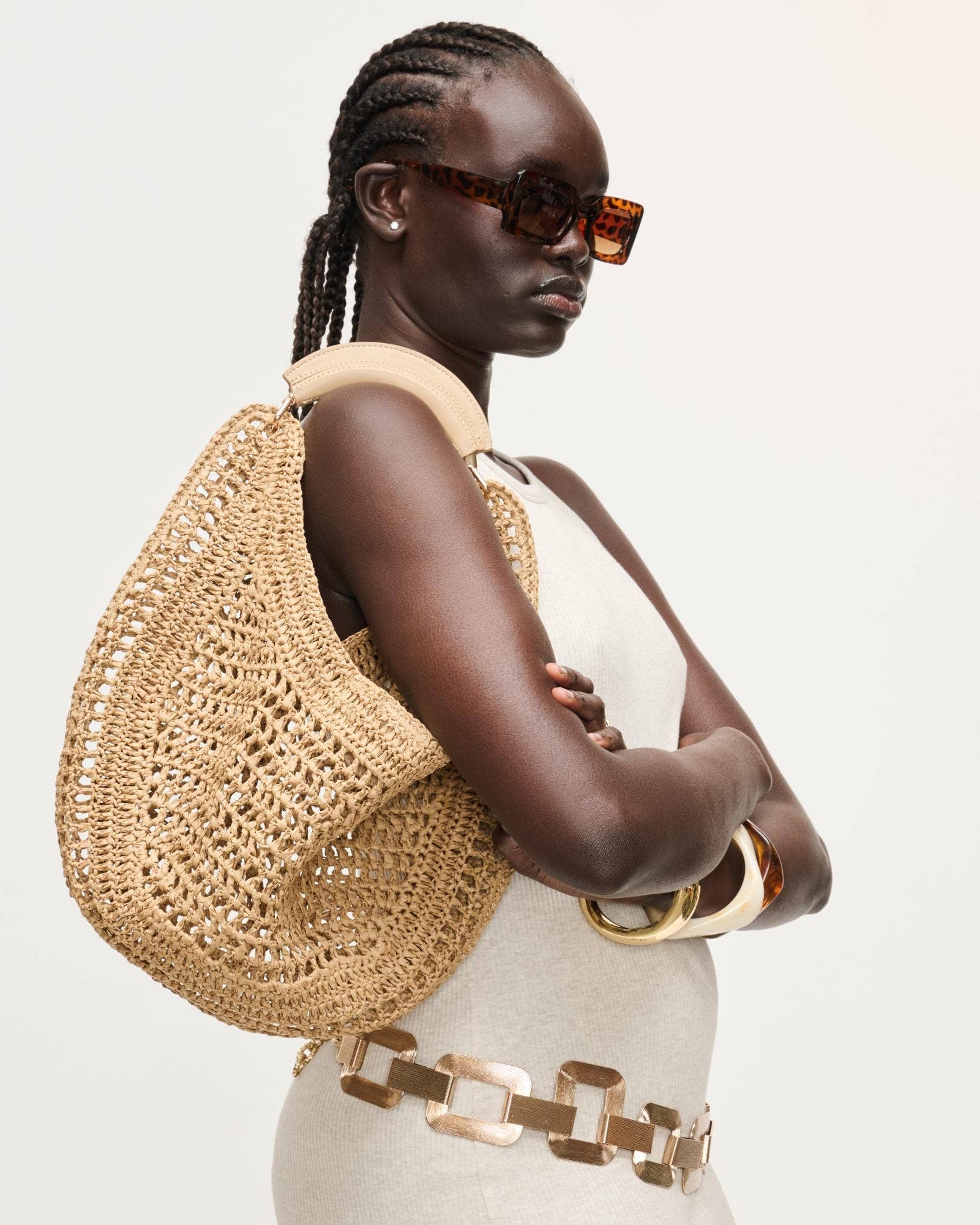 Woman with braided hair wearing sunglasses and a straw bag on a light background