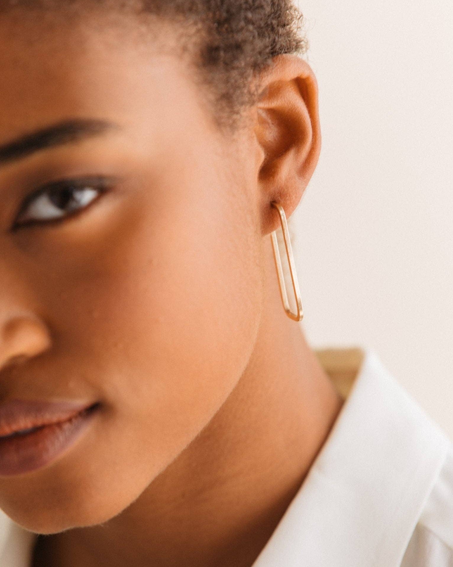 Close-up of a person wearing a gold hoop earring with a neutral background