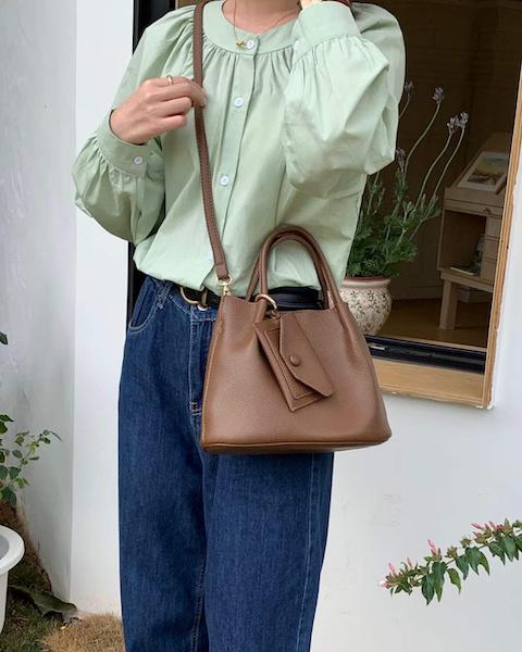 Person wearing a light green blouse and blue jeans, holding a brown handbag.
