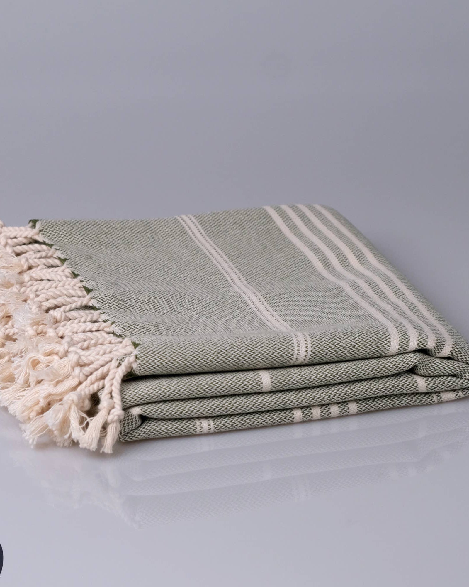 Stack of folded green and white striped towels with tassels on a gray background, featuring the Kallbadon brand.