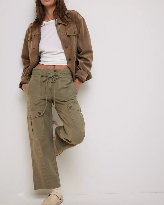 Woman wearing a brown jacket and green cargo pants against a white background