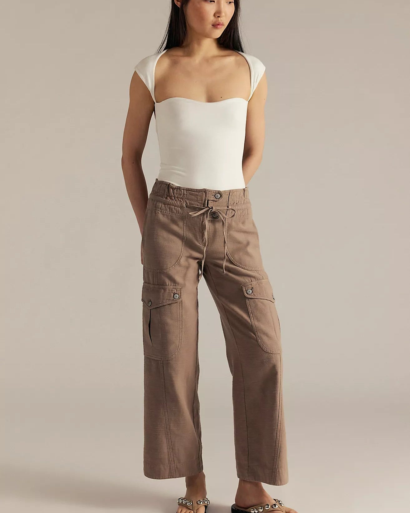 Woman wearing a white top and brown cargo pants on a beige background