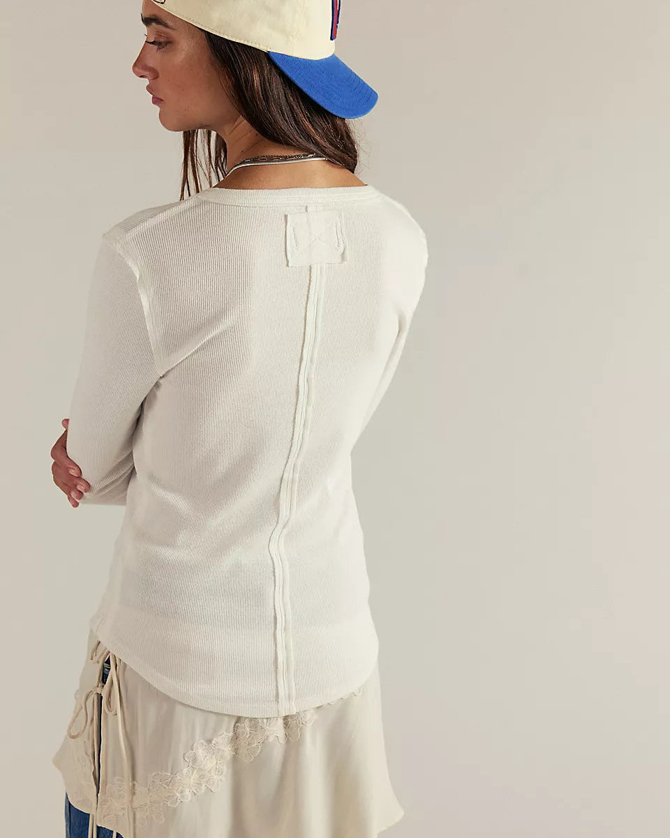 Person wearing a white long-sleeve top with a blue cap on a plain background