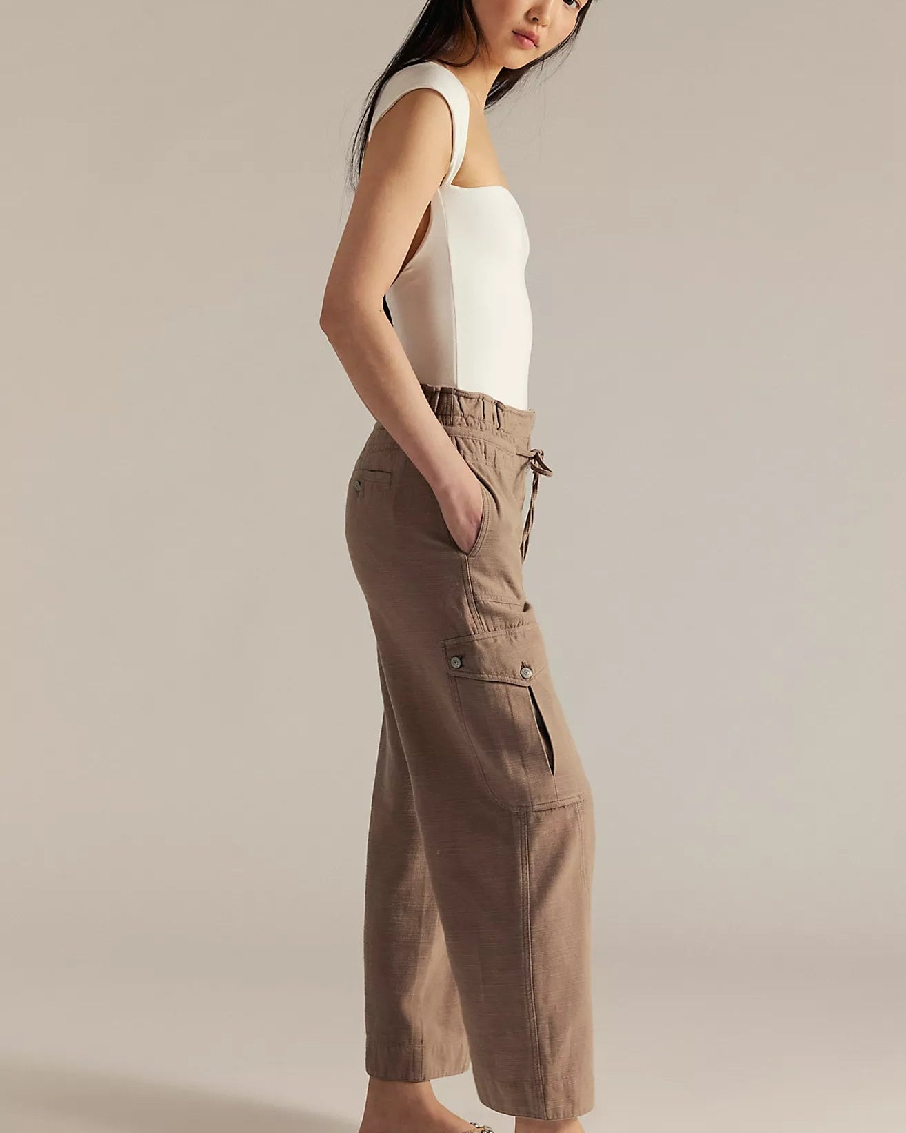 Woman wearing a white sleeveless top and beige cargo pants on a plain background
