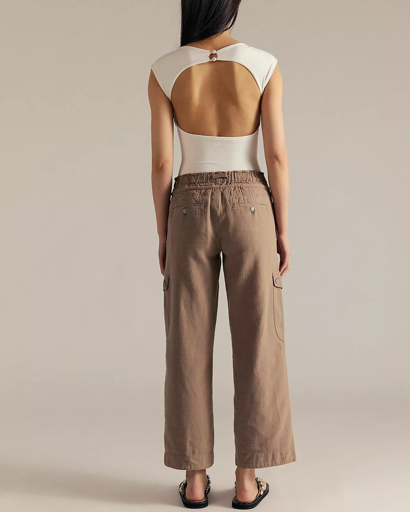 Person wearing a white sleeveless top and brown pants on a beige background