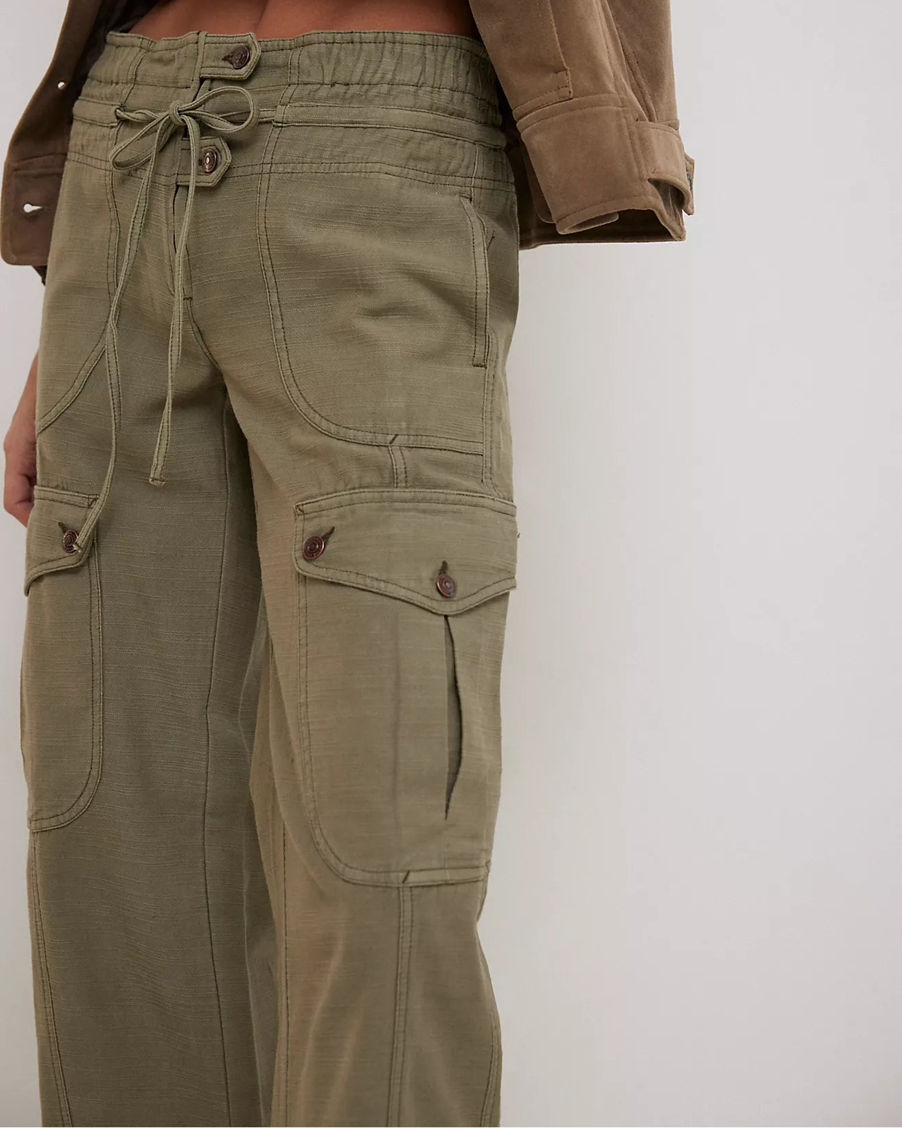 Person wearing olive green cargo pants with a brown jacket on a white background