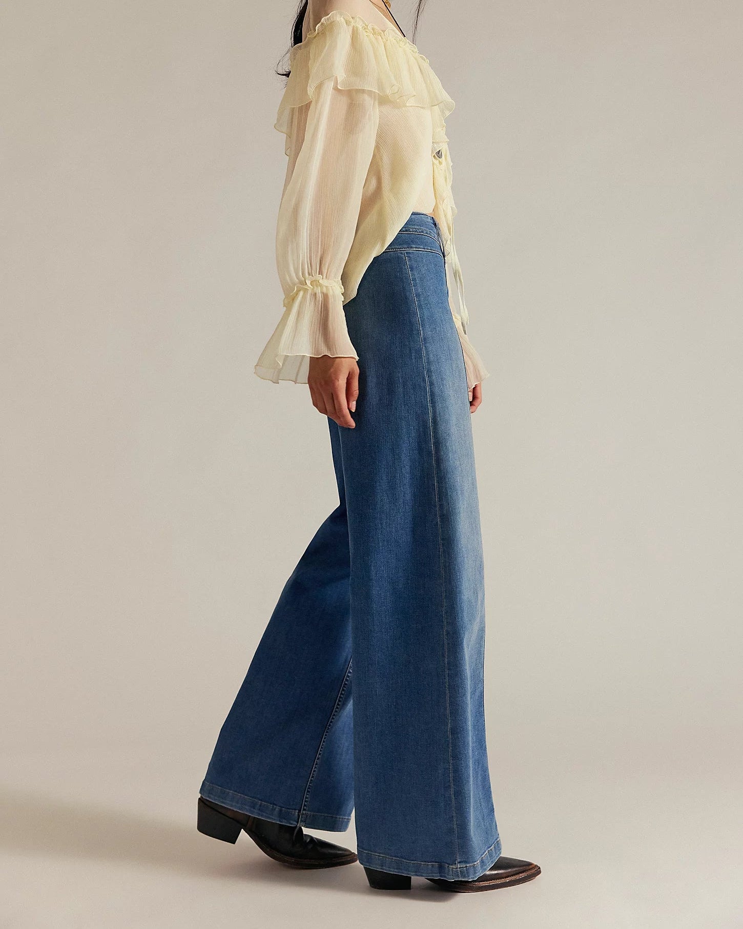 Woman wearing a light yellow blouse and blue jeans on a plain background