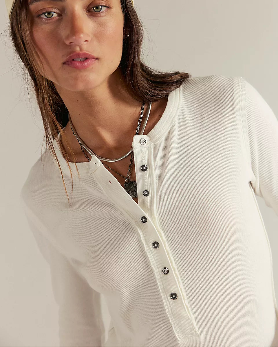 Person wearing a beige cap and white shirt with black buttons on a neutral background