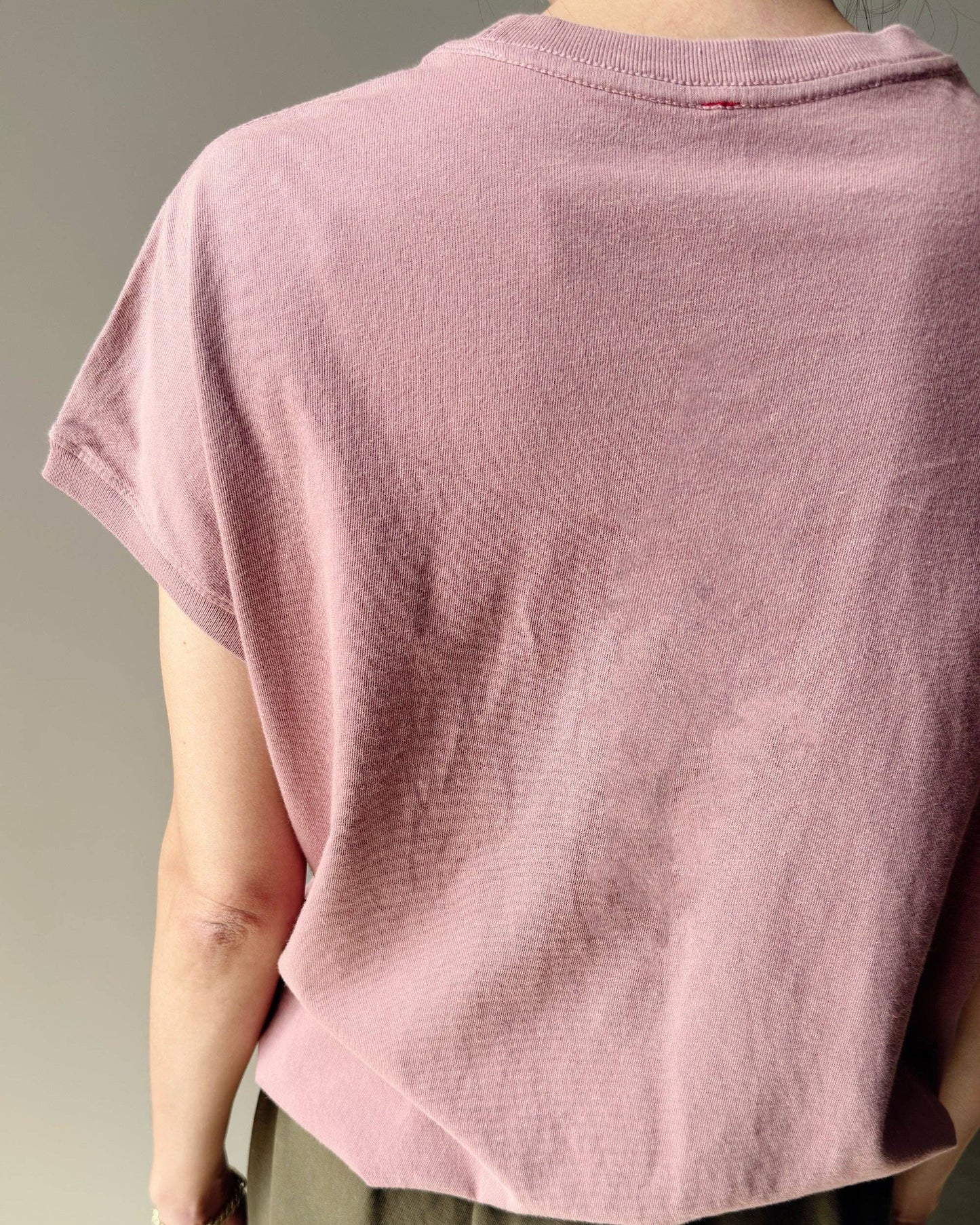 Person wearing a loose-fitting pink t-shirt and green pants against a neutral background