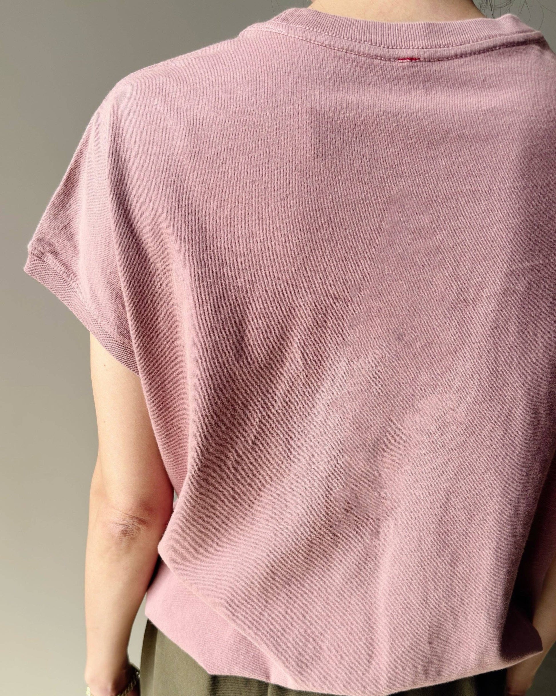 Person wearing a loose-fitting pink t-shirt and green pants against a neutral background