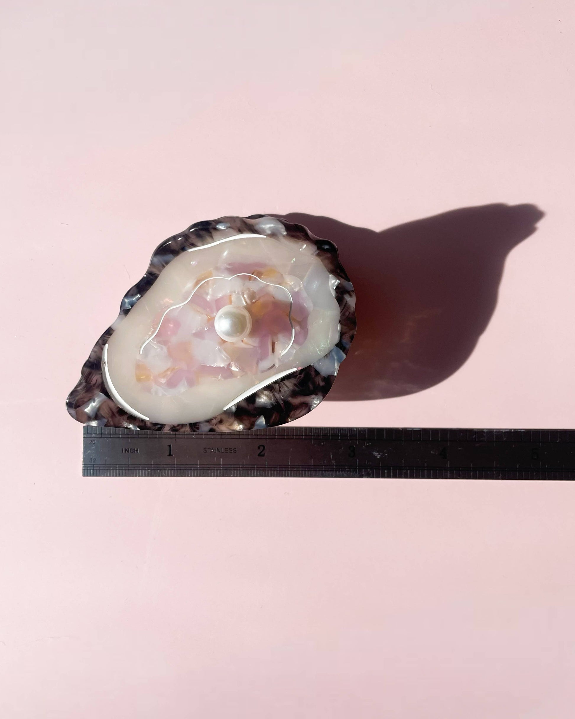 Oyster hair clip with a pearl inside on a pink background