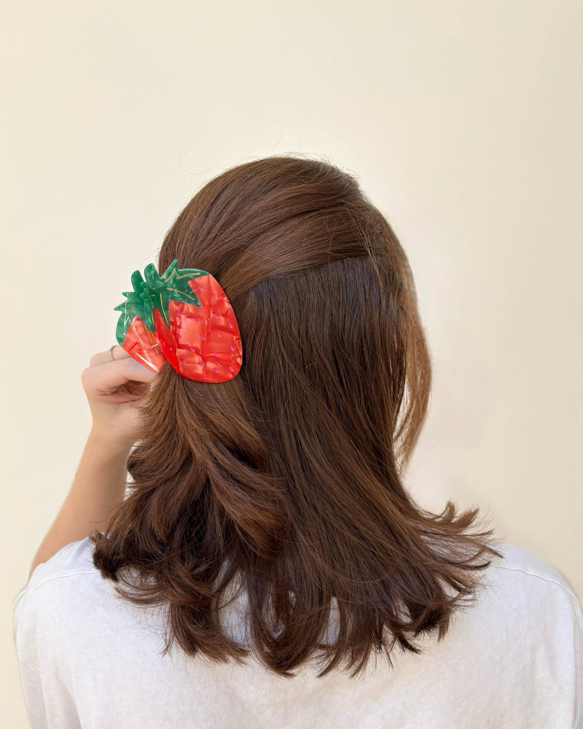 Person wearing a strawberry-shaped hair clip on a plain background