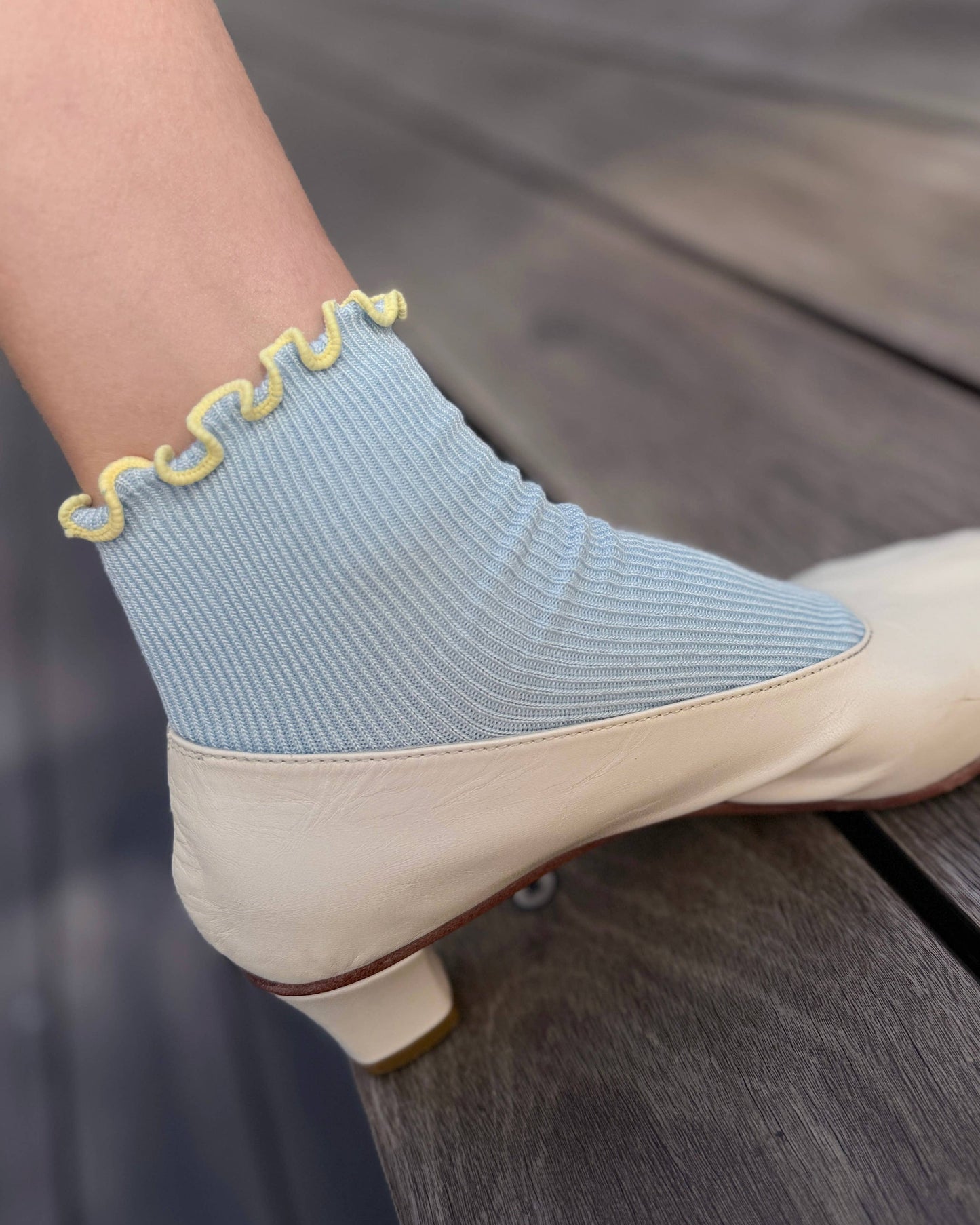 Light blue sock with yellow trim worn over a beige shoe on a wooden surface