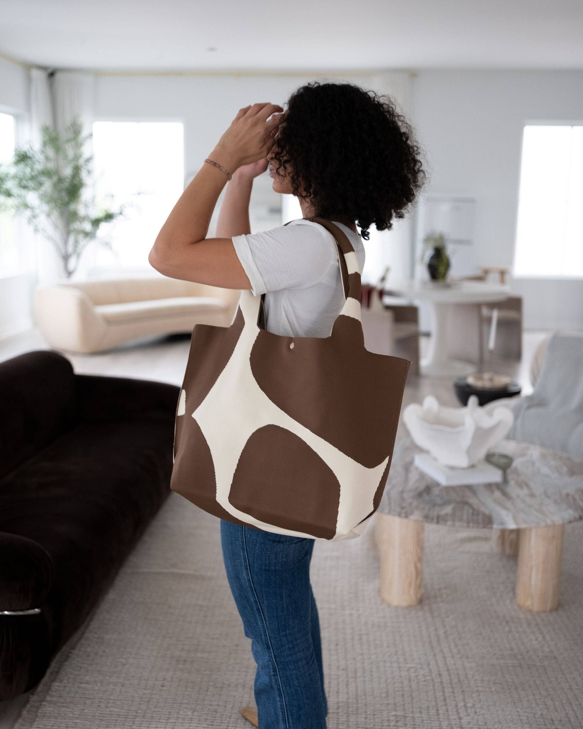 Person holding a brown and white patterned bag in a modern living room.
