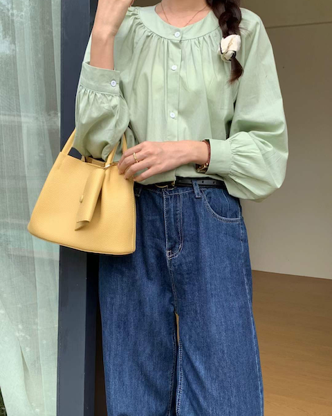 Person wearing a light green blouse and blue jeans, holding a yellow handbag.