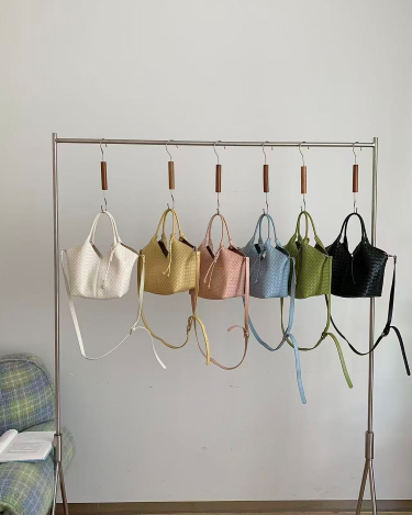 Metal clothing rack with various colorful handbags against a plain wall.